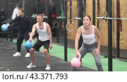 Concentrated athletic young woman taking part in intense group training in modern gym, performing exercises with kettlebells. Fitness and bodybuilding concept. Стоковое видео, видеограф Яков Филимонов / Фотобанк Лори