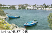 Serene view of blue waters and neatly moored boats along coastline near Punic Ports in Carthage, against backdrop of modern city architecture under Tunisian sun. Стоковое видео, видеограф Яков Филимонов / Фотобанк Лори