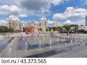 Маленькая девочка бегает между струй фонтана на Центральной площади Зеленограда. На фоне новый жилой массив. Голубое небо, белые облака. (2024 год). Редакционное фото, фотограф Сергей Никифоров-Гордеев / Фотобанк Лори