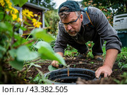 A plumber leaned over a sewer well on the territory of a village house. Septic tank maintenance. Стоковое AI-изображение, AI-художник Коханова Наталья / Фотобанк Лори