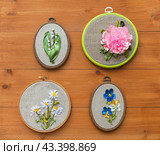 Four types of spring garden flowers are embroidered with satin ribbons in hoop on wooden background. Daisies, pansies, lilies of valley and peony. Embroidery as hobby and leisure. Gifts for Mothers Day. Стоковое фото, фотограф Виктория Катьянова / Фотобанк Лори