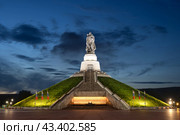 Мемориал Воину-освободителю, город Кемерово, Кемеровская область — Кузбасс, Россия. На фоне тёмного вечернего неба большая освещённая фигура советского солдата с мечом, держащего на руке спасённую им немецкую девочку. Памятник установлен в городе Кемерово в 2022 году. Является копией монумента Воину-освободителю в берлинском Трептов-парке. (2023 год). Редакционное фото, фотограф Андрей Степанов / Фотобанк Лори
