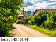 Дорога в деревне на фоне высотного жилого комплекса (2024 год). Редакционное фото, фотограф Илья Старков / Фотобанк Лори