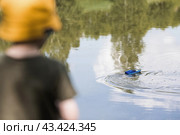 A 5-year-old boy in a yellow panama hat launches a radio-controlled boat in a pond. Children's fun and street games. Child's leisure time. Стоковое фото, фотограф Photojuli / Фотобанк Лори