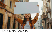 A young woman on a city street shows a large empty sign above her head. Street protests and demonstrations concept, banner with copy space. Стоковое AI-изображение, AI-художник Александр Довянский / Фотобанк Лори