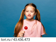 Portrait of happy cheerful little girl lick chupa-chups candy enjoy sweet snack wear good look clothes isolated over blue color background. Стоковое фото, фотограф Ирина Михайличенко / Фотобанк Лори