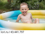 It's a hot day. A cute boy is swimming and splashing in the pool. A happy little boy smiles at the camera. Splashes of water are flying in all directions. The concept of summer holidays with children. Стоковое фото, фотограф Photojuli / Фотобанк Лори
