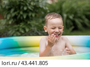 It's a hot day. A cute boy is swimming and splashing in the pool. A happy little boy smiles at the camera. Splashes of water are flying in all directions. The concept of summer holidays with children. Стоковое фото, фотограф Photojuli / Фотобанк Лори