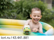 It's a hot day. A cute boy is swimming and splashing in the pool. A happy little boy smiles at the camera. Splashes of water are flying in all directions. The concept of summer holidays with children. Стоковое фото, фотограф Photojuli / Фотобанк Лори