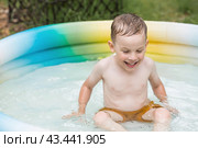 It's a hot day. A cute boy is swimming and splashing in the pool. A happy little boy smiles at the camera. Splashes of water are flying in all directions. The concept of summer holidays with children. Стоковое фото, фотограф Photojuli / Фотобанк Лори