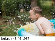 It's a hot day. A cute boy is swimming and splashing in the pool. A happy little boy smiles at the camera. Splashes of water are flying in all directions. The concept of summer holidays with children. Стоковое фото, фотограф Photojuli / Фотобанк Лори