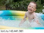 It's a hot day. A cute boy is swimming and splashing in the pool. A happy little boy smiles at the camera. Splashes of water are flying in all directions. The concept of summer holidays with children. Стоковое фото, фотограф Photojuli / Фотобанк Лори