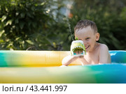 It's a hot day. A cute boy is swimming and splashing in the pool. A happy little boy smiles at the camera. Splashes of water are flying in all directions. The concept of summer holidays with children. Стоковое фото, фотограф Photojuli / Фотобанк Лори