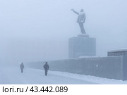Зима в Якутске. Республика Саха (Якутия), Сибирь, Россия. Вид на заснеженную городскую улицу и памятник Владимиру Ленину. По тротуару вдоль ограды идут прохожие. Очень холодная зимняя погода в январе. Плохая видимость из-за густого морозного тумана. Суровый сибирский климат (2024 год). Редакционное фото, фотограф Андрей Степанов / Фотобанк Лори