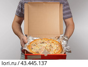 A man in a striped gray T-shirt holds an open red pizza box offering to take it. Стоковое фото, фотограф Дмитрий Львович Алферов / Фотобанк Лори