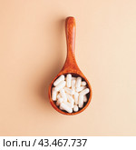 Top view of wooden spoon filled with white capsules on beige background, square composition. Стоковое фото, фотограф Юлия Трикашная / Фотобанк Лори