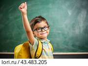 A boy with glasses shows the class with his hand. The child goes to school for the first time. A child with a school bag and a book. A child in the classroom on the background of a blackboard. Back to school. Стоковое AI-изображение, AI-художник Photojuli / Фотобанк Лори