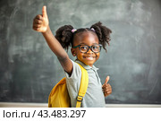 A cute black African American girl with glasses shows the class with her hand. The child goes to school for the first time. A child with a school bag and a book. A child in the classroom on the background of a blackboard. Back to school. Стоковое AI-изображение, AI-художник Photojuli / Фотобанк Лори