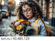 A cute little curly-haired girl with glasses and a bouquet of autumn flowers goes to school for the first time. A child with a school bag, a book and flowers. A child on a city street. Back to school. Стоковое AI-изображение, AI-художник Photojuli / Фотобанк Лори