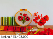 Handmade embroidery with satin ribbons of poppy flowers in hoop, bouquet of fresh red poppies in vase on wooden table. Nearby is set of colorful satin ribbons, needles and scissors for work. DIY concept, beautiful still life. Стоковое фото, фотограф Виктория Катьянова / Фотобанк Лори