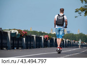 Молодой мужчина едет на электрическом самокате по велодорожке. (2024 год). Стоковое фото, фотограф Rashpil / Фотобанк Лори