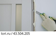 Cut off excess hardened polyurethane foam with a knife after foaming the cracks in the door frame. Construction and repair. Installation and fastening of a wooden frame. Стоковое видео, видеограф Дмитрий Кобзев / Фотобанк Лори