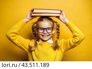 A pretty girl with glasses and books on her head. The child goes to school for the first time. A child on a yellow monochrome background. Back to school. Стоковое AI-изображение, AI-художник Photojuli / Фотобанк Лори