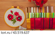 Video of floral hand embroidery with satin ribbons of poppy flowers in hoop, bouquet of fresh red poppies on wooden table. Nearby is set of colorful satin ribbons, needles and scissors for craft. Flat lay, close-up. Стоковое видео, видеограф Виктория Катьянова / Фотобанк Лори
