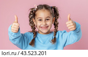Young girl with pigtails in blue sweatshirt showing thumbs up. Стоковое AI-изображение, AI-художник Юрий Поздников / Фотобанк Лори