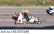 Road workers in orange vests apply markings to a city asphalt road using a special painting machine on a sunny day. Road repair and improvement concept. Стоковое фото, фотограф Виктория Катьянова / Фотобанк Лори