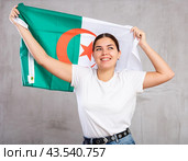 Joyous young woman holding Algeria flag against unicoloured background. Стоковое фото, фотограф Яков Филимонов / Фотобанк Лори