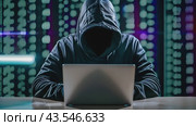 A hooded figure sits at a desk in a dark room, using a laptop. The background features blue lights and a graph on a screen. Стоковое AI-видео, аниматор Данила Большаков / Фотобанк Лори