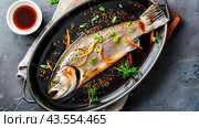 Marinated raw trout. Whole fish in bowl with soy sauce, sesame seeds and herbs. Ready to be cooked. Top view. Стоковое AI-изображение, AI-художник Алеся Цапенко / Фотобанк Лори