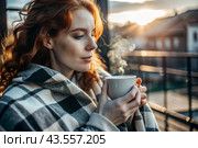 Autumn evening. A red-haired, beautiful woman wrapped in a plaid with a mug of hot coffee on a beautiful patio in the rays of the setting sun. The girl inhales the aroma of the drink. Romance, comfort and harmony. Стоковое AI-изображение, AI-художник Photojuli / Фотобанк Лори
