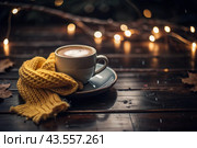 A seasonal drink. Delicious hot cappuccino in a mug with a saucer and a knitted snood, a scarf on a wooden table in the interior of the cafe. It's a rainy autumn day. Стоковое AI-изображение, AI-художник Photojuli / Фотобанк Лори