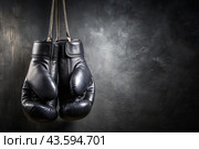 Professional black boxing gloves hang on a black background with a space to copy. Стоковое AI-изображение, AI-художник Photojuli / Фотобанк Лори