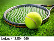 A yellow tennis ball and a tennis racket are lying on the lawn. A summer sport. Great tennis. Стоковое AI-изображение, AI-художник Photojuli / Фотобанк Лори
