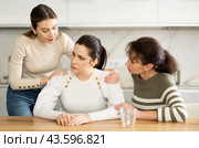 Sad woman sits silently in kitchen, adult girls sympathize and comfort her. Стоковое фото, фотограф Яков Филимонов / Фотобанк Лори
