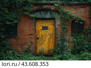 An old brick wall overgrown with dense green plants. In the center of the wall is a peeling yellow door with a metal window. To the right of the door are two small windows with metal bars, partially obscured by vines and ivy. The scene looks abandoned and mysterious, creating the atmosphere of a secluded place hidden from prying eyes. Стоковое AI-изображение, AI-художник Анна Кривицкая / Фотобанк Лори