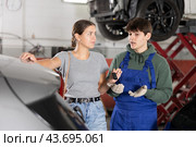 Smiling female client giving car keys to young mechanic in workshop. Стоковое фото, фотограф Яков Филимонов / Фотобанк Лори