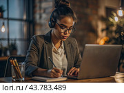 A young female freelance businessman in glasses and headphones is working on a laptop or shopping in an online store. The woman is writing something in a notebook. Стоковое AI-изображение, AI-художник Photojuli / Фотобанк Лори