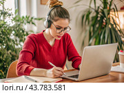 A young female freelance businessman in glasses and headphones is working on a laptop or shopping in an online store. The woman is writing something in a notebook. Стоковое AI-изображение, AI-художник Photojuli / Фотобанк Лори