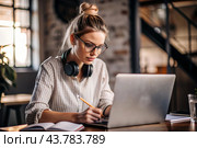 A young female freelance businessman in glasses and headphones is working on a laptop or shopping in an online store. The woman is writing something in a notebook. Стоковое AI-изображение, AI-художник Photojuli / Фотобанк Лори