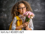 A sweet, beautiful first-grader girl with glasses. In the hands of a bouquet of flowers. The child goes to school for the first time. A child with a backpack, a book and flowers. Back to school. Стоковое AI-изображение, AI-художник Photojuli / Фотобанк Лори