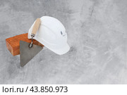 Bricklayer tools - trowel, bricks and white helmet on cement background. copyspace. Стоковое фото, фотограф Павел Муравьев / Фотобанк Лори