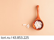 Wooden spoon with white capsules on beige background, top view. Стоковое фото, фотограф Юлия Трикашная / Фотобанк Лори