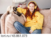 Peaceful teen girl in modern headphones sit relax on comfortable couch listening to music. Стоковое фото, фотограф Гладских Татьяна / Фотобанк Лори