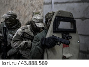 Группа военных в камуфляже выстроилась за солдатом с бронещитом и пистолетом у бетонной стены. Подготовка к штурму. (2020 год). Редакционное фото, фотограф Евгений Зимин / Фотобанк Лори