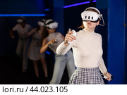 Emotional girls in VR headsets fully immersed in game, engaged in virtual reality world, manipulating objects or shooting targets with joysticks in hands. Стоковое фото, фотограф Яков Филимонов / Фотобанк Лори
