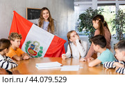 Positive female teacher discussing with preteens students state flag of Peru in auditory of middle school. Стоковое фото, фотограф Яков Филимонов / Фотобанк Лори